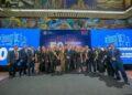 Group of about 20 professionals in formal attire posing for a group photo at a 50th anniversary event, with large blue banners that read '50 Aniversario' and 'Gobierno de Monterrey' in the background.